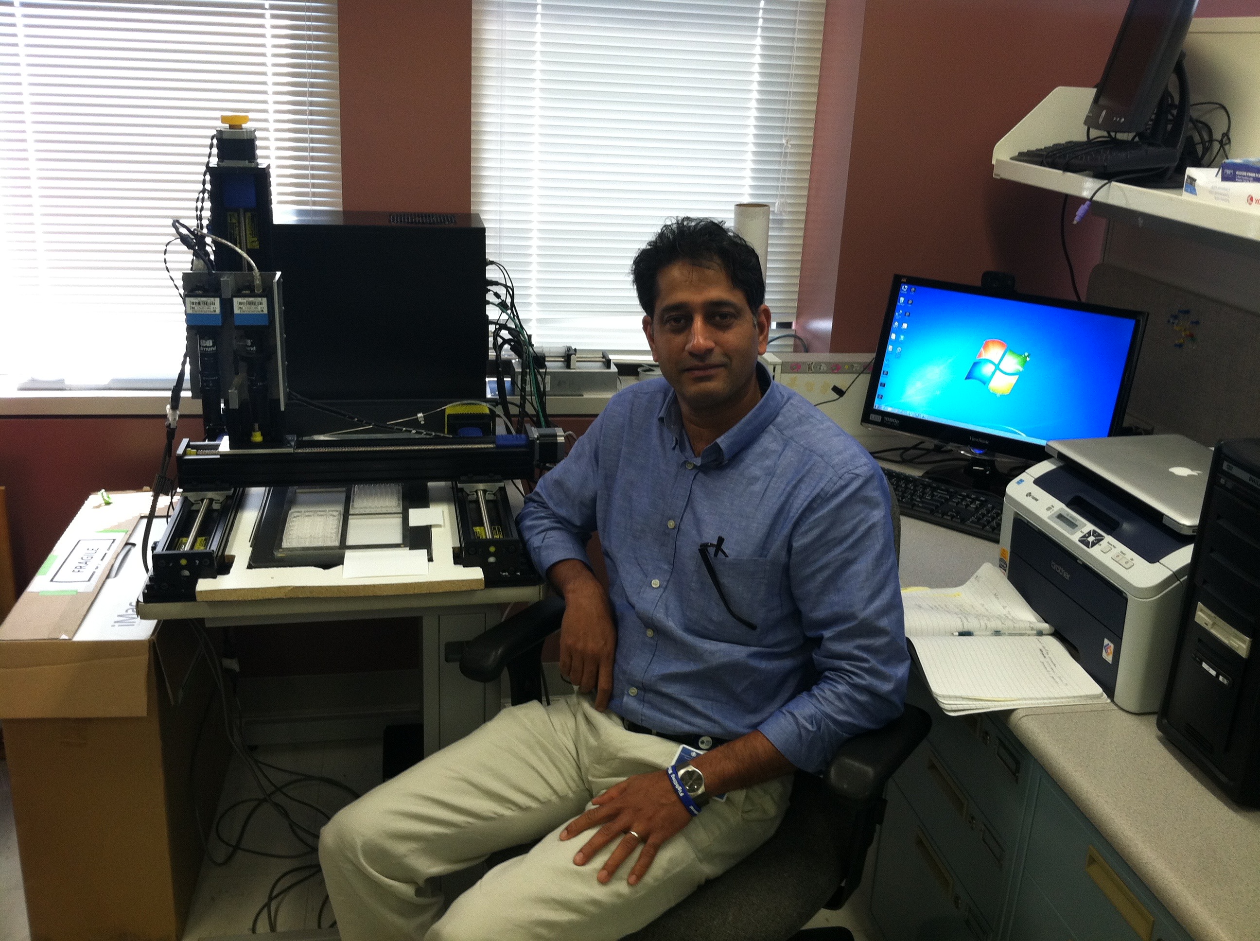 Royce Mohan with the automated vascular patterning assay system, featuring an XYZ positioning table, machine vision cameras, and a computer-controlled syringe for high-throughput drug discovery screening